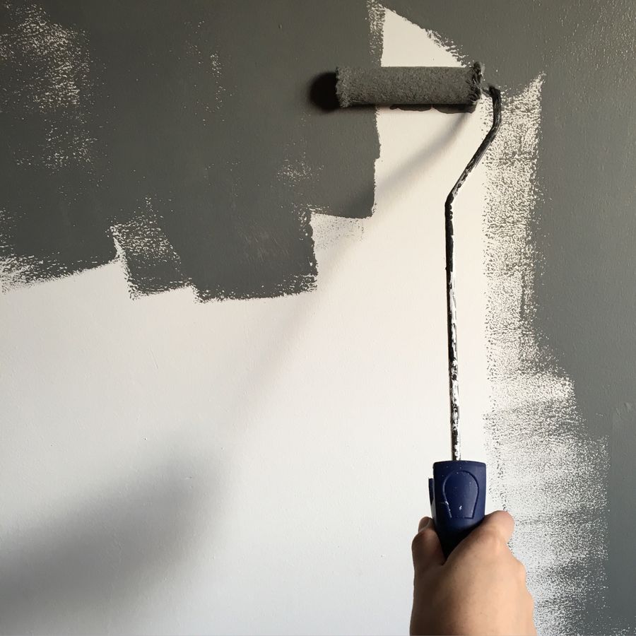 A hand painting an interior wall with a roller